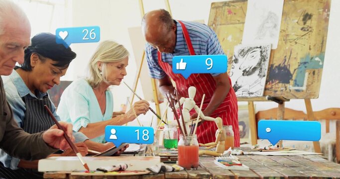 Working mature adults mixing paint on canvases at wooden studio table, with tablet and paintbrushes