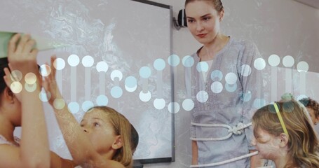 Educator guiding six children around table at whiteboard in class, with green block and DNA overlay