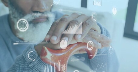 Senior man pressing red anatomical bone model at office desk, with digital data overlays