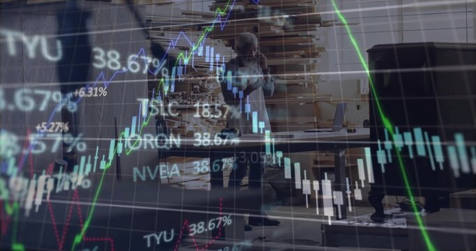 Holding smartphone to ear man tracking stock market graphics at woodshop, with planks and laptop - Powered by Adobe