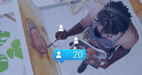 Naklejka premium Painting artist wearing apron applying color to canvas on easel in studio with brush and reference