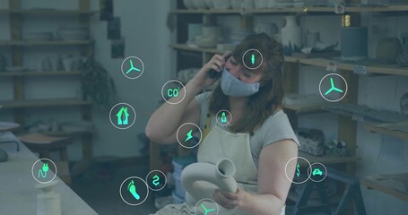 Holding clay vessel, apron-clad ceramic artist talking on smartphone at workshop, with energy icons