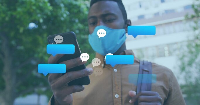 Man wearing cloth mask and backpack, walking on urban path holding smartphone with chat bubbles - Powered by Adobe