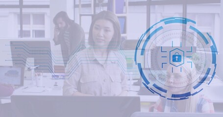 Standing woman in beige shirt scanning two monitors at open-plan office, with security lock overlay