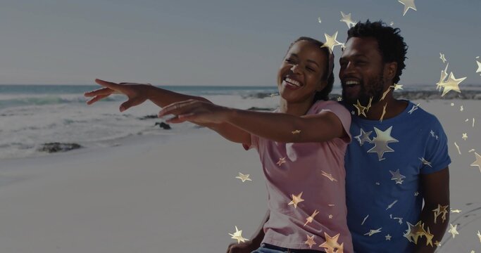 Spreading arms smiling couple sitting on sandy beach in t-shirts, with star-shaped graphic overlays