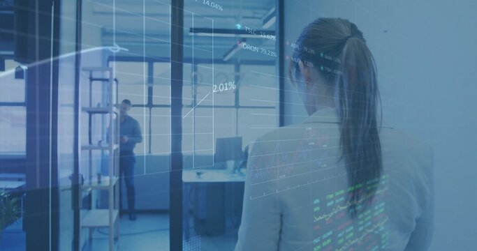 Analyst wearing business attire studying transparent interface with stock tickers at modern office