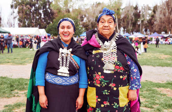 Mapuche women smiling and wearing traditional attire with silver necklaces outdoor