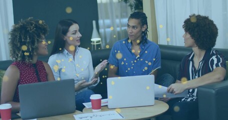 Collaborating four-person office team meeting in casual lounge, with laptops and red coffee cups