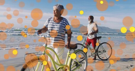 Pushing senior woman guiding pale green cruiser bicycle along sandy shoreline, with artistic filter