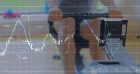 Rowing man in workout gear pulling rower handle toward chest at gym, with digital financial charts