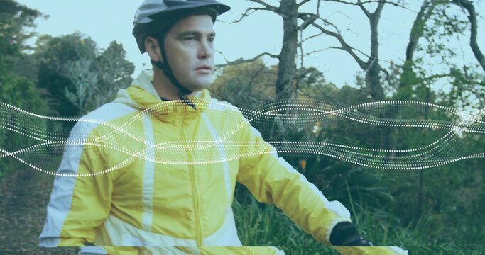 Riding light-skinned cyclist pedaling forest trail, with helmet, windbreaker, handlebars and gloves