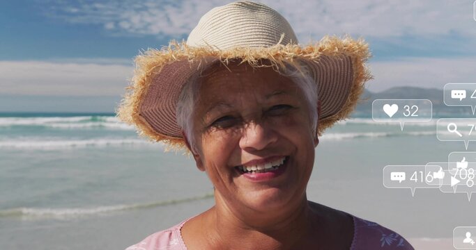Smiling senior woman wearing straw sun hat and pink floral top at beach, floating reaction icons - Powered by Adobe