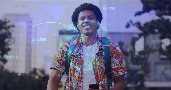 Male walking on sidewalk at dusk wearing floral shirt and backpack holding smartphone and earphones