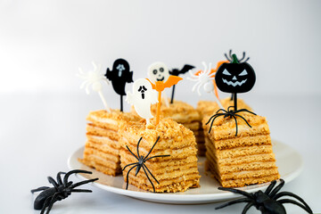Slices of honey cake for a Halloween party, each adorned with fun and creepy toppers. Decorative black spiders creates a perfect mysterious and celebratory mood. Close-up. Selective focus.