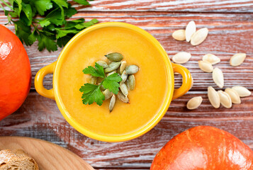 Autumn comfort food, seasonal pumpkin soup in a yellow bowl, garnished with fresh parsley leaves and pumpkin seeds. Warm and cozy fall atmosphere. Close-up. Top view.