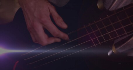 Plucking musician's right hand moving across metal strings bass guitar in purple light, lens flare