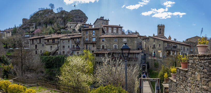 Photograph of the charming medieval village of Rupit. The image shows its stone houses with wooden balconies and flowers, cobblestone streets, and its mountainous natural surroundings, reflecting the 