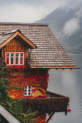 A small cottage with sloping roofs on the edge of the lake, covered in autumn leaves on its facade