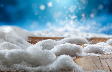 Wooden surface covered with snow with empty copy space for product placement with blurred dark blue frosty winter snowing background. Seasonal advertising, nature, winter concept.
