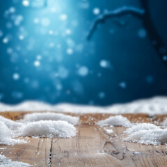 Wooden surface covered with snow with empty copy space for product placement with blurred dark blue frosty winter snowing background. Seasonal advertising, nature, winter concept.