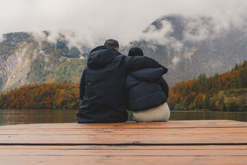 Couple sitting on the edge of a dock watching the lake and enjoying their rural tourism trip on a rainy autumn day