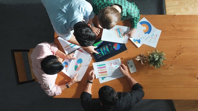 Top down aerial view of smart business people analyze data together at meeting. Group of business team working together and looking at financial chart at tablet placed on meeting table. Convocation.