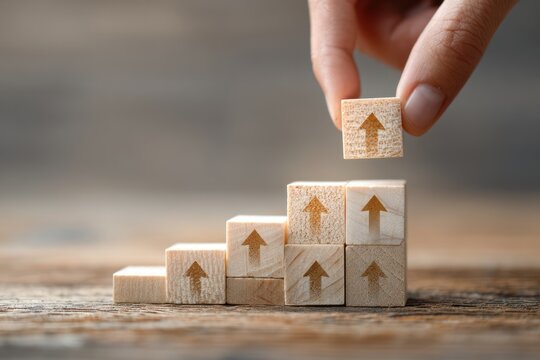 Human hand building a staircase of wooden blocks with arrows pointing upwards showing financial or personal growth