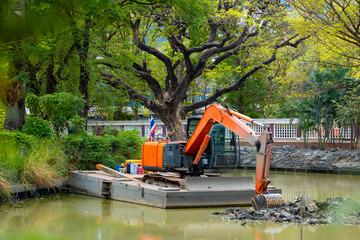 Excavator on floating platform clearing pond in Thailand park