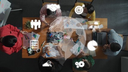 A diverse team engages in a collaborative meeting focused on business strategies using charts, laptops, and global icons, reflecting teamwork and innovation in a professional environment. Raster