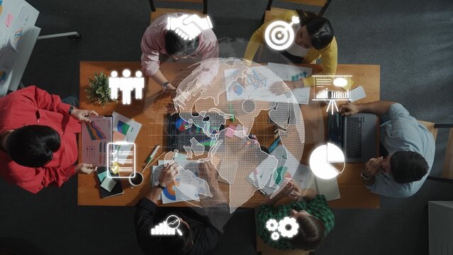 A diverse team engages in a collaborative meeting focused on business strategies using charts, laptops, and global icons, reflecting teamwork and innovation in a professional environment. Raster