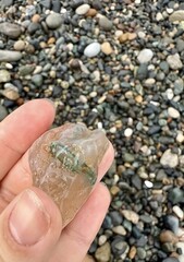 Hand Holds Clear Agate Stone Found on Rocky Beach Shoreline