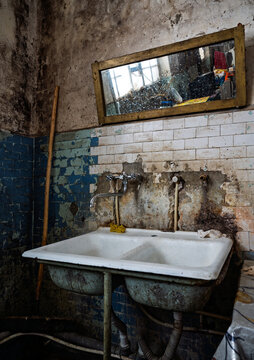 Grungy double sink in old bathroom with cracked tiles and dirty mirror.