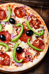 Pizza with chorizo ​​sausage, mozzarella cheese, green pepper and black olives. Rustic wooden background. Soft focus.	