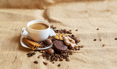 A white cup with a saucer and coffee and coffee beans on a brown cloth background