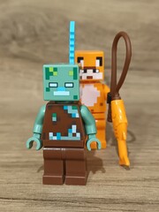 Fototapeta premium Whimsical block figures a pink pig-like character with a golden weapon and a grey animal holding a fresh carrot, posed on wood, symbolizing fantasy play and imaginative adventure