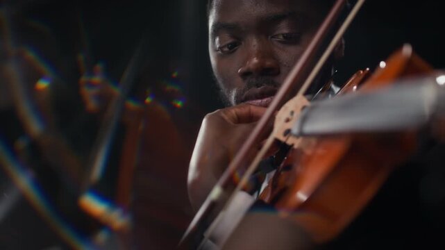 Close up motion blur shot of young adult African American male musician playing violin against black background during symphonic orchestra concert, slow motion