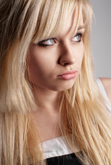 Naklejka premium Close-up portrait of young woman with blonde hair and thoughtful, displeased gaze. Her eyes look off into the distance. Simplistic background highlights her features.
