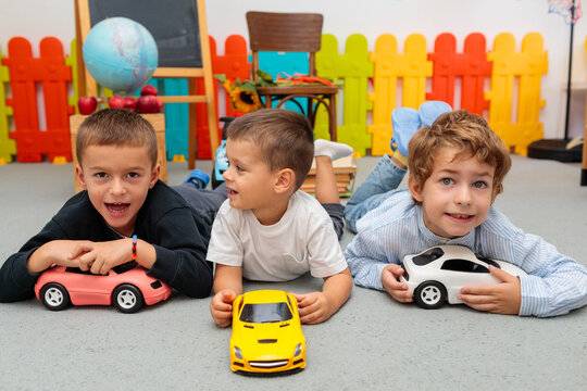 three boys lying on the floor in a classroom and playing with toy cars, having fun and smiling for the camera. friendship, brotherhood, and a joyful childhood - Powered by Adobe