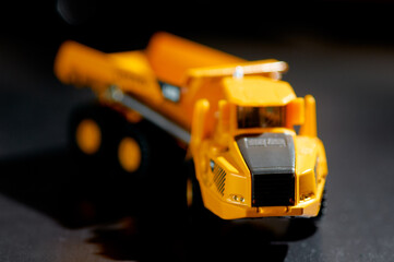Yellow toy dump truck on a dark surface, emphasizing vibrant colors and miniature detail. Dark...