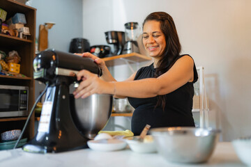 Smiling pregnant woman using stand mixer in home kitchen
