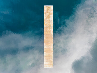 Abstract top-down drone view of a wooden pier dividing serene blue lake water and cloud reflections in Estonia.