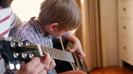 Handsome dad teaches his cute son to play the guitar sitting on sofa in the living room at home. Happy Father's Day. Father teaching his child to play guitar. Kid Learning music skill. Art education - Powered by Adobe