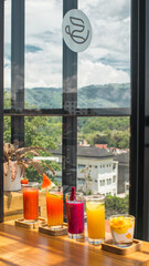 Assortment of colorful fruit juices on a wooden counter with a scenic view.