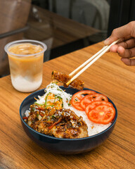 A bowl of rice with toppings and a drink on a wooden table.