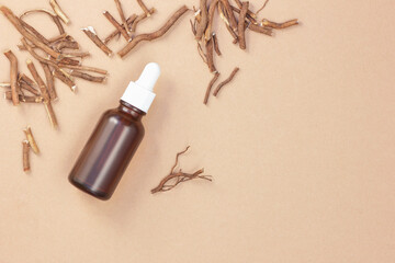Root oil on flat background with dried roots nearby, copy space, natural medicine, natural cosmetic for hair, skin care, stress therapy, from above overhead top view