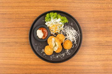 Overhead shot of a black plate with fried balls and condiments.