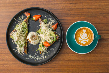 Overhead shot of avocado toast, coffee, and strawberries on a wooden table.