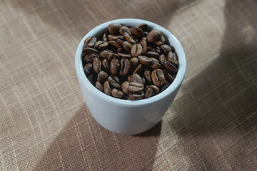 White ceramic mug filled with roasted coffee beans on a rustic brown cloth