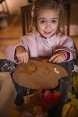 Young girl creating art with leaves and paper during indoor activity on a cozy afternoon