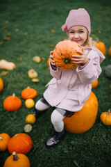 Happy child with pumpkin enjoys autumn day at a farm surrounded by harvest decorations